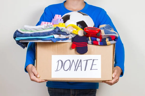 Donation concept. Kid holding donate box with clothes, books and toys
