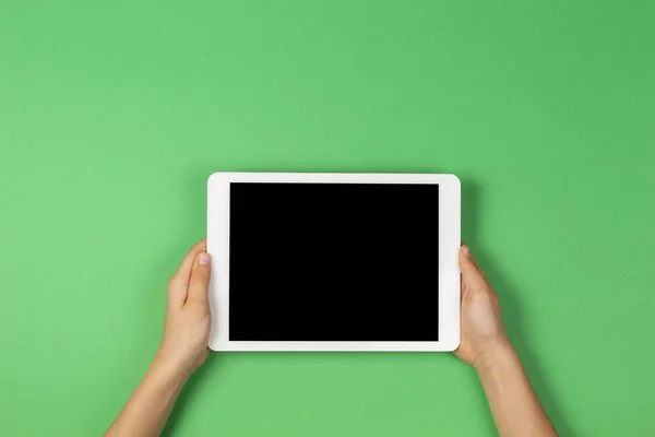 Açık yeşil arkaplanda tablet bilgisayarı tutan çocuk elleri
