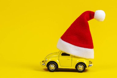 Noel arkaplanı. Sarı arka planda küçük kırmızı Noel Baba şapkalı eski model bir araba.