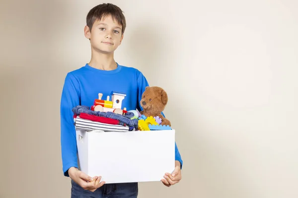 Concepto de donación. Niño sosteniendo donar caja con libros, ropa y juguetes —  Fotos de Stock