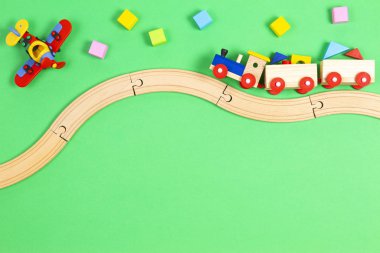 Ahşap demiryolunda renkli blokları olan tahta oyuncak tren ve açık yeşil arka planda kırmızı uçak.