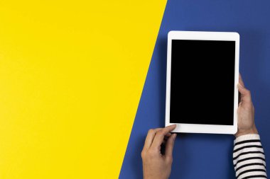 Lacivert ve sarı arka planda dijital tablet bilgisayarı olan kadın eller. Üst görünüm