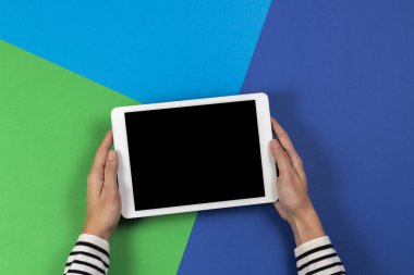 Lacivert ve açık yeşil arka planda dijital tablet bilgisayarı olan kadın eller. Üst görünüm