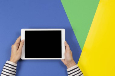 Mavi sarı ve açık yeşil arka planda dijital tablet bilgisayarı olan kadın eller. Üst görünüm