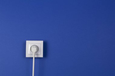 Mavi donanma arka planında elektrik prizine takılı beyaz kablo