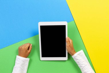 Eller tablet bilgisayarı sarı, mavi ve yeşil arka planda. Üst görünüm