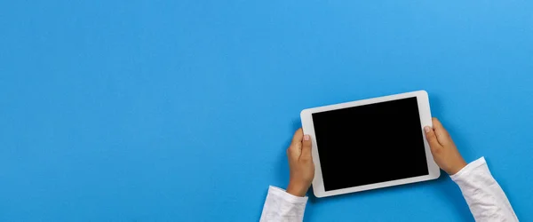 Açık mavi arka plan üzerinde beyaz tablet bilgisayar tutan çocuk el — Stok fotoğraf