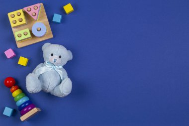 Bebek çocukların oyuncak geçmişi. Mavi oyuncak ayı, piramit kulesi istifleme, şekil tanıma bulmacası istifleyici ve lacivert arka planda renkli bloklar. Üst görünüm