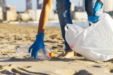 Plastikten temiz plaj. Plajdan plastik şişe çöplerini toplayıp geri dönüşüm için plastik torbaya koyuyorlar.