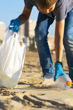 Plastik çöpten şehir plajını temizliyorum. Çocuk plajdan plastik şişe çöplerini topluyor ve geri dönüşüm için plastik torbaya koyuyor.