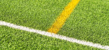 Yeşil suni çimen sahası futbol sahasının gerisinde beyaz ve sarı çizgili. Üst görünüm