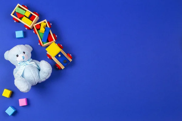 Bebê crianças brinquedos fundo. Trem de madeira, urso de pelúcia azul e blocos coloridos no fundo azul marinho — Fotografia de Stock