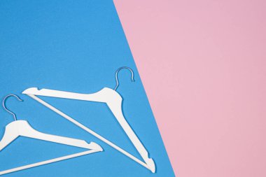 Pastel pembe ve mavi arka plan üzerinde iki beyaz ahşap giysi askıları. Alışveriş, satış, promosyon, sosyal medya, yeni sezon konsepti