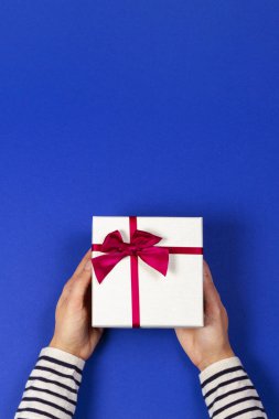 Kadının elleri hediye kutusunu tutuyor. Mavi kurdeleyle bağlanmış. Üst görünüm, metin için yer. Tatil kavramı