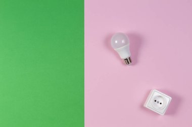Yeşil ve açık pembe arka planda beyaz elektrik prizi ve ampul. Üst görünüm