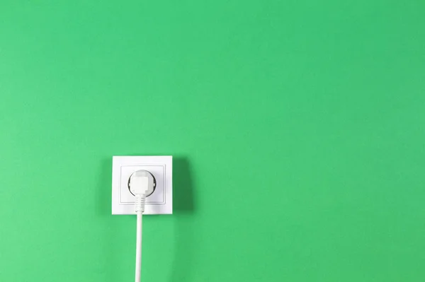 Cable blanco conectado al enchufe eléctrico sobre fondo de color verde — Foto de Stock
