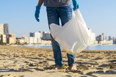 Clean beach from plastic. Volunteer picking up plastic bottle trash from the beach and putting into plastic bag for recycle