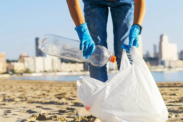 Clean beach from plastic. Volunteer hands picking up plastic bottle trash from the beach and putting into plastic bag for recycle