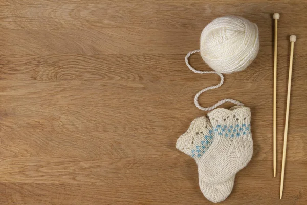 Knitting background. Wooden knitting needles, ball of yarn and small wool knitted socks on wooden background — 스톡 사진