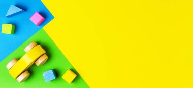 Geometrik sarı mavi yeşil arka planda renkli blokları olan ahşap kırmızı oyuncak araba. Üst görünüm