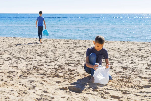 Sukarelawan membersihkan pantai dari plastik. Anak laki-laki berjalan di pantai dan mengambil sampah botol plastik dan dimasukkan ke dalam kantong plastik untuk didaur ulang — Stok Foto