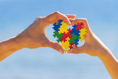 Çocuk ve yetişkin eller mavi gökyüzü arka planında renkli kalpleri tutuyorlar. Dünya otizm farkındalık günü konsepti
