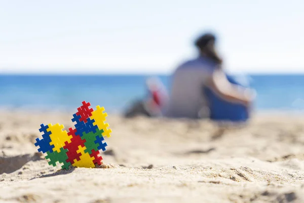 Autismo consapevolezza giorno concetto. Puzzle cuore sulla sabbia e la silhouette della madre abbracciare il bambino sulla spiaggia e guardando verso l'oceano mare — Foto Stock