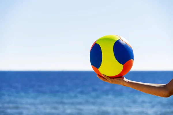 Ręczne gospodarstwa kolorowa piłka na plaży z błękitnym morzu i tle nieba — Zdjęcie stockowe