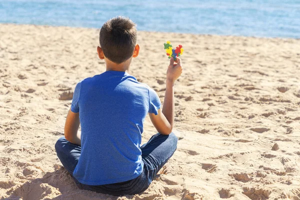 Menino sentado na praia, olhando para o mar oceano e segurando colorido autismo coração consciência — Fotografia de Stock
