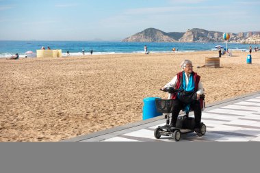 Benidorm, Spain - February 25, 2020: Woman with mobility scooter in Levante beach area in Benidorm, Spain