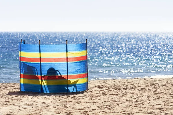 Due persone che si rilassano dietro il colorato parabrezza a strisce Spiaggia di Poniente sul Mar Mediterraneo a Benidorm, Spagna — Foto Stock