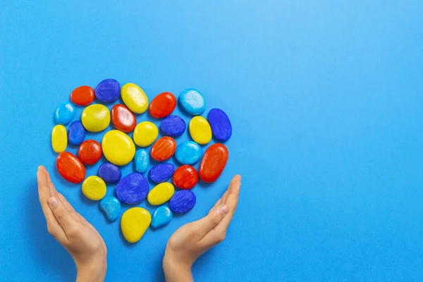 World autism awareness day concept. Child hands with heart made of blue yellow red color stones over light blue background — Stock Photo, Image