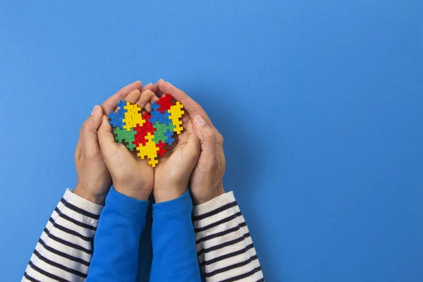 世界の自閉症意識の日の概念。大人と子供の手保持パズルハート上のライトブルーの背景 — ストック写真