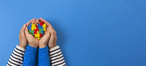 Concepto del Día Mundial del autismo. Adulto y niño manos sosteniendo el corazón del rompecabezas sobre fondo azul claro — Foto de Stock