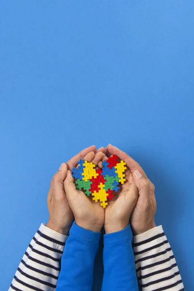 Concepto del Día Mundial del autismo. Adulto y niño manos sosteniendo el corazón del rompecabezas sobre fondo azul claro —  Fotos de Stock