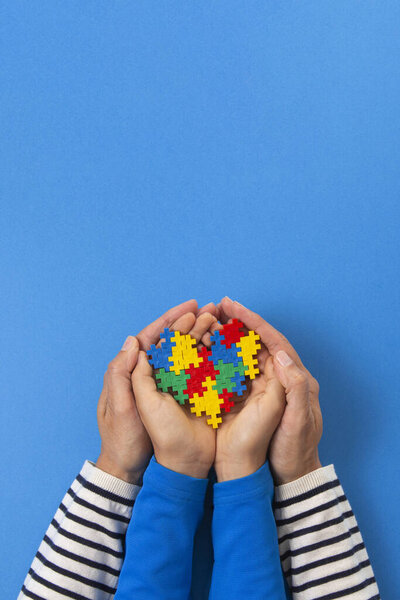 World autism awareness day concept. Adult and child hands holding puzzle heart on light blue background