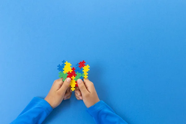 Journée mondiale de sensibilisation à l'autisme concept. Mains d'enfant tenant coeur puzzle coloré sur fond bleu — Photo