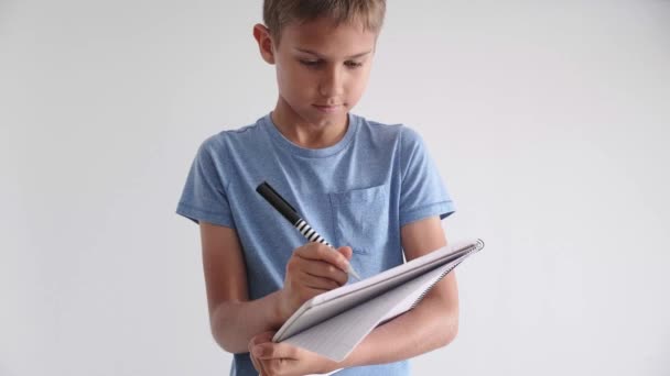 Мальчик-подросток стоит и держит в руках спираль школьные тетради упражнения тетрадь и писать заметки с ручкой — стоковое видео