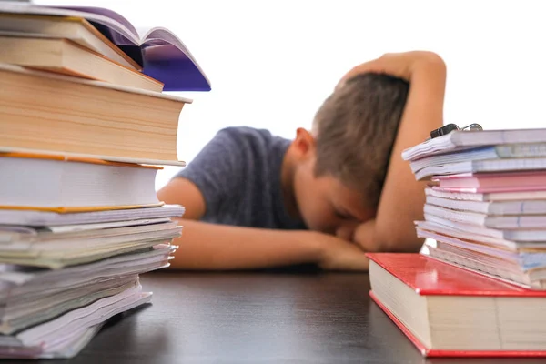 Okul ödevi için yığınla kitap ve hayal kırıklığına uğramış okul çocuğunun masada oturarak başını eğmesi. — Stok fotoğraf
