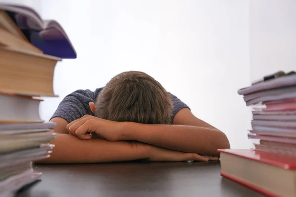 Cansado estudante decepcionado baixando a cabeça sentado entre pilha de livros, livros didáticos, livros de exercícios escolares em sua mesa em casa — Fotografia de Stock