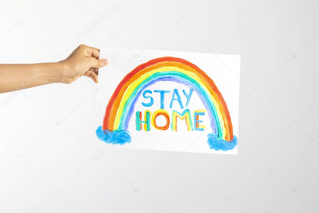Kid hand holding drawing picture with colorful rainbow and words Stay home. Social media campaign for coronavirus prevention