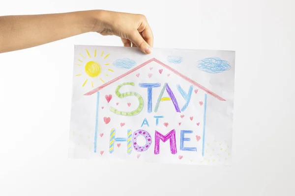 Cuarentena en casa durante la pandemia de coronavirus. Mano de niño sosteniendo dibujo con palabras Quédese en casa. Campaña de medios sociales para la prevención del coronavirus — Foto de Stock