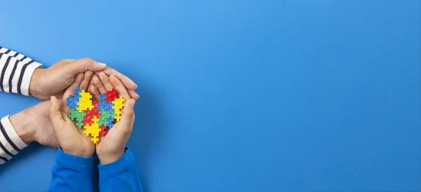 Dünya otizm farkındalık günü konsepti. Yetişkin ve çocuk elleri açık mavi arka planda yapboz kalbini tutuyor