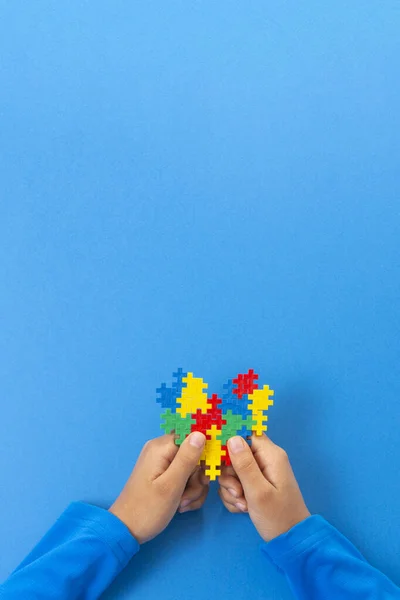 Journée mondiale de sensibilisation à l'autisme concept. Mains d'enfant tenant coeur puzzle coloré sur fond bleu — Photo