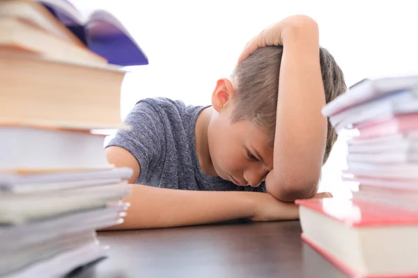 Fatigué écolier déçu abaissant la tête assis au milieu d'une pile de livres, manuels, cahiers d'exercices scolaires sur son bureau à la maison — Photo