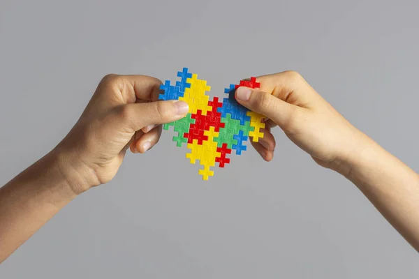 Światowy Dzień Świadomości Autyzmu. Dzieci ręce gospodarstwa kolorowe serce puzzle nad jasnoszarym tle — Zdjęcie stockowe