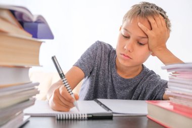 Öğrenci çocuk kitap yığınlarının arasında oturuyor, ders kitapları, çalışma kitapları masasında ve ödevlerini yapıyor. Eğitim, online mesafe öğrenimi, evde karantina sırasında evde eğitim