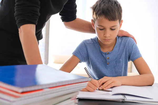 Kid sitting at the table with many books notebooks and doing homework. Mother helping him. Learning difficulties, learning at home, education, motivation concept — Stock Photo, Image