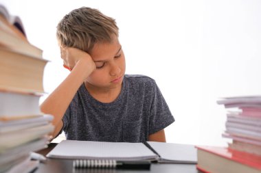 Öğrenci çocuk kitap yığınlarının arasında oturuyor, ders kitapları, çalışma kitapları masasında ve ödevlerini yapıyor. Eğitim, online mesafe öğrenimi, evde karantina sırasında evde eğitim