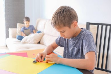 Eğitim, çevrimiçi öğrenme, evde girişim. Çocuk renkli kağıtlardan kağıt yapıyor. Kardeşim evde online ders için tablet bilgisayar kullanıyor.
